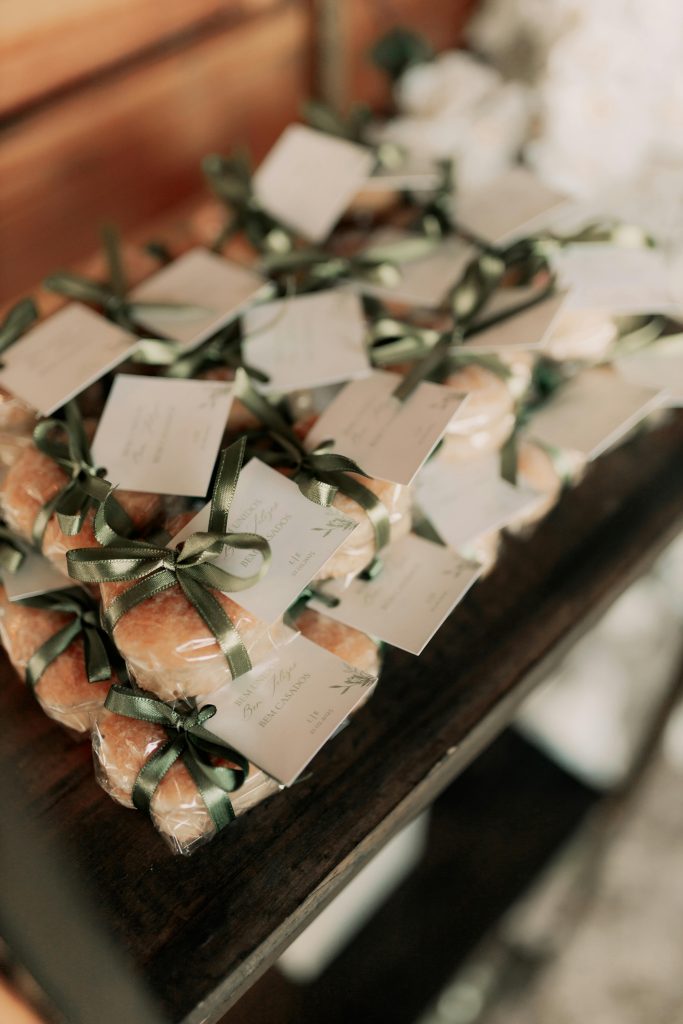 Stack of beautifully wrapped wedding favors with green ribbons and tags on a wooden table.