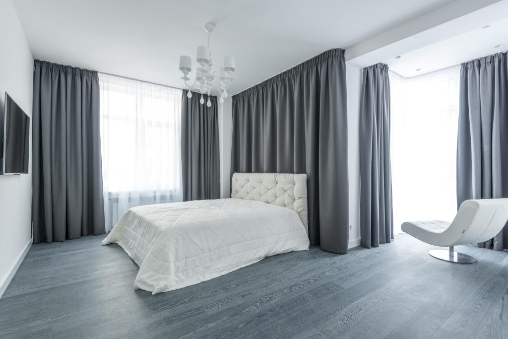 Bright minimalist bedroom featuring gray curtains, white bed, and sleek decor.